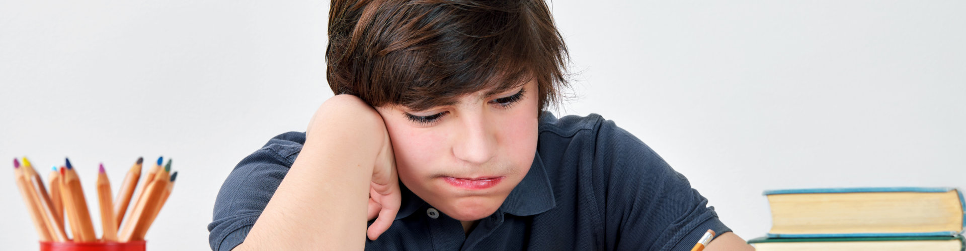 Bored and exhausted teenage boy sitting at the desk and concentrate on his homework